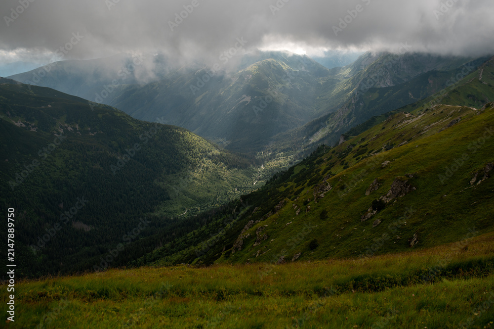 Fototapeta premium Sunbeams breaking through clouds over a green mountain valley