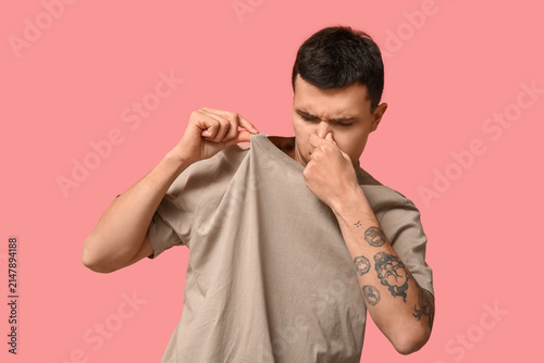 Cuadro en lienzo Handsome young man feeling bad smell from dirty clothes on pink background
