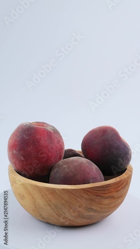 Whole peaches in wooden bowl rotate against white background with space for text. Sweet summer fruits, organic peaches for eating or juicing. Agricultural advertising, healthy eating. 4k vertical 