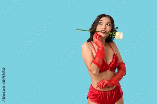Young Asian woman in sexy underwear with beautiful white rose on blue background