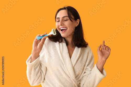 Young woman in bathrobe with razor on yellow background