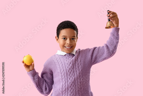 Little African-American schoolboy with bell and apple on pink background