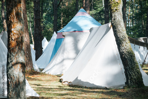 Obraz na plátně A group of white tents is set up under the trees in a forest, suggesting a medieval encampment