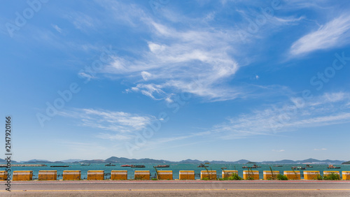 Blue Sky and White Clouds Above Coastal Road with Yellow Concrete Barrier Blocks
