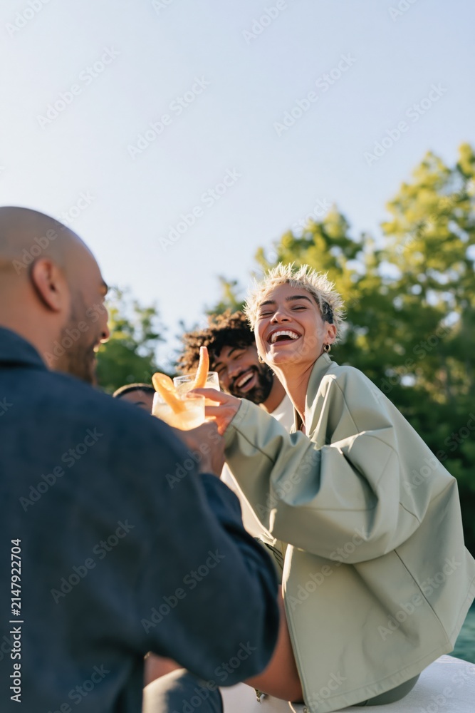 Obraz premium Laughing friends sharing drinks outside in daylight for summer social banner and lifestyle background design