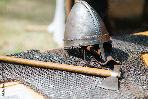 Konstfotografi A medieval helmet rests on a chainmail sheet next to a wooden battle axe