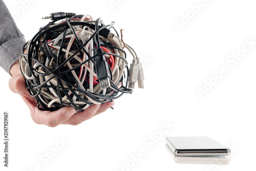Close-up hands holding tightly wound bundle of black, white, and red cables with visible plugs above smartphone on clean white background, showing messy connectivity, technology clutter, and need