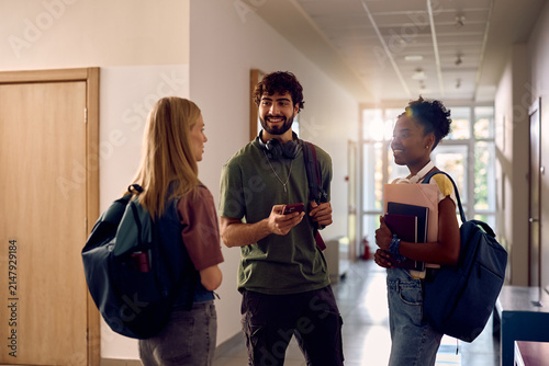 Happy college student talking to female friends in hallway.