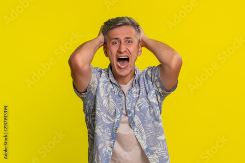 Middle-aged man shouting aggressively with wide hand gestures and furious expression, expressing strong anger and heated argument. Young guy showing emotional outburst isolated on yellow background.