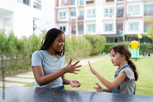African female caregiver playing with Caucasian young girl outdoors in park. 