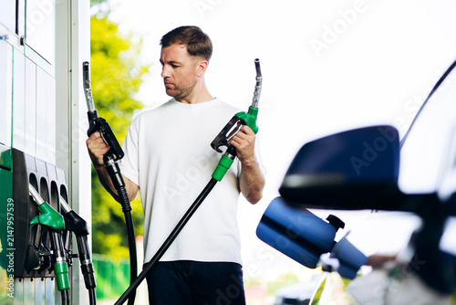Obraz na plátně Man holding two fuel nozzles, making a choice at a gas station while refueling a