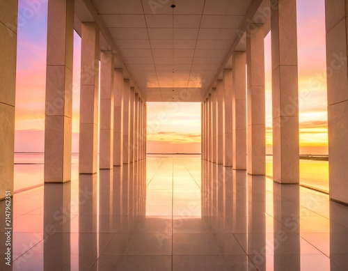 A symmetrical colonnade frames a vibrant sunrise, reflecting on polished flooring
