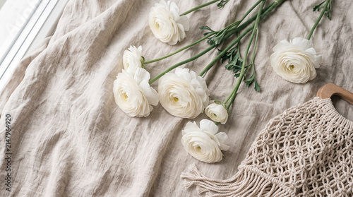 Elegant flat lay with white flowers on natural linen fabric. Soft daylight, neutral tones and organic textures create a calm botanical composition with copy space and minimalist aesthetic.
