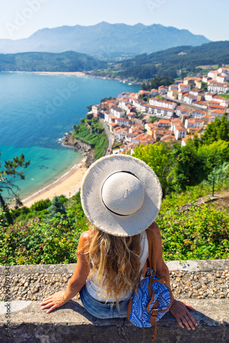 woman wearing straw hat sitting enjoying panoramic view of lastres coastal village in asturias spain