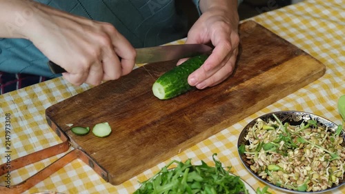 Food prep. Female hands slicing cucumber for salad on wooden board. 
