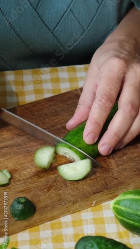 Vertical video. Food prep. Female hands slicing cucumber for salad on wooden board. 
