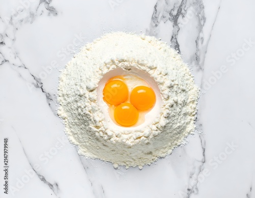 Overhead view Flour mound with three egg yolks nested on a marbled surface