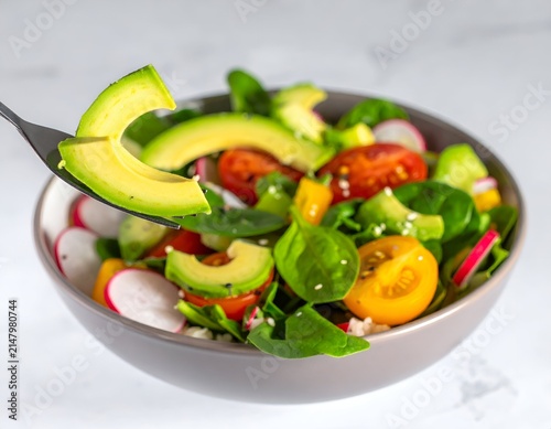 Close-up of a vibrant healthy salad bowl with avocado on a fork, white backdrop