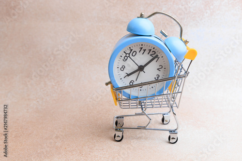 фотографія Blue alarm clock in a shopping cart on a simple background with focus on time an