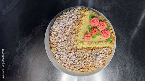 Top view of a homemade celebration cake decorated with buttercream roses and chopped peanuts on a white plate. Elegant festive dessert for birthdays, parties, holiday. Confectionery themes.