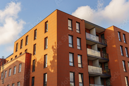 Modern red brick residential apartment building exterior at sunset, featuring detailed masonry, balconies and windows against a blue sky