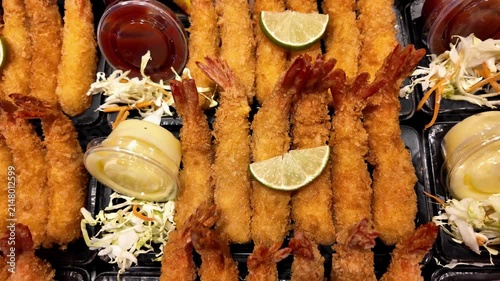 Close-up of crispy breaded shrimp platters served with lemon wedges, fresh salad and dipping sauces at a Thai street food market. Golden fried seafood ready to eat, beautifully presented for takeaway.