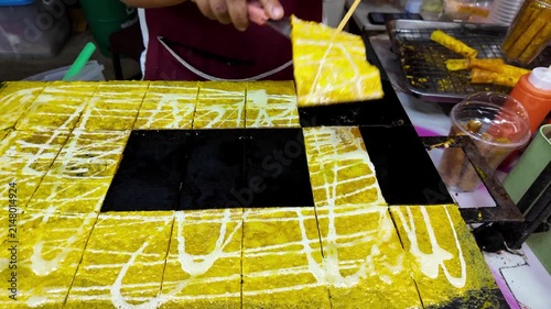 Fresh Thai crispy coconut wafer rolls being cooked, cut and rolled on a hot griddle by a street food vendor at a night market. Traditional sweet dessert prepared in front of customers. 4K horizontal v