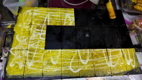 Traditional Thai crispy coconut wafer rolls being cooked on a large hot griddle and carefully rolled by a street food vendor at a busy night market. Authentic Thai dessert prepared fresh in front of c