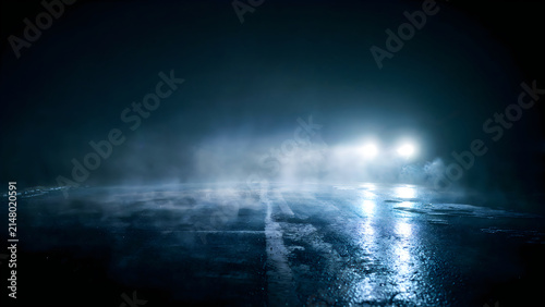 Car headlights on a dark foggy road at night. Vehicle driving through mist on wet asphalt.