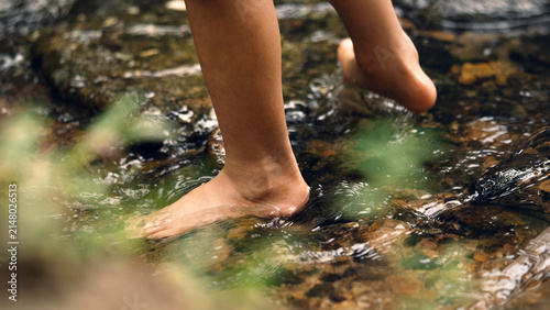 Photography Close-up of a barefoot child walking through a shallow forest stream over smooth rocks, enjoying grounding, sensory play, outdoor exploration, and a natural connection with the environment