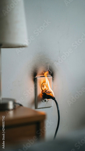 Dangerous electrical socket fire starting on wall near nightstand lamp with electrical electricity emergency malfunction incident defective residential accident connection overload interior