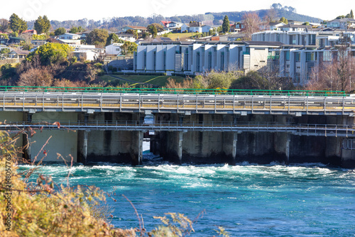 Control Gates bridge at Taupō, New Zealand, regulating water flow from Lake Taupō to Waikato River, supporting downstream hydroelectric generation. Suburb of Nukuhau in background.