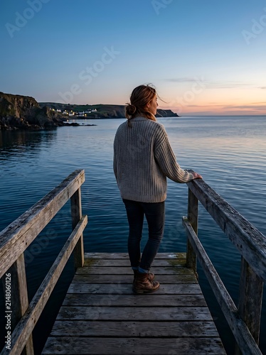 Woman on dock overlooking coastal sunset cliffs.