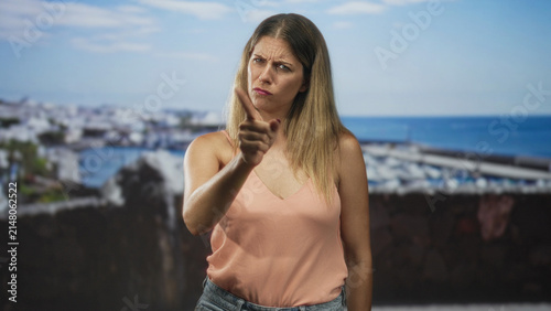 Foto Woman pointing finger at camera in studio with seaside backdrop, furrowed brow and stern posture suggesting accusation; anger scolding
