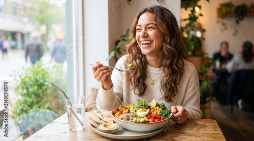 Young smiling woman eating a fresh salad in a cozy cafe