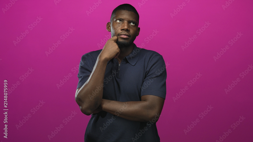 Obraz premium Man with hand to chin and arm crossed, looking up with palm raised and slight shrug in magenta studio; thoughtful uncertainty.