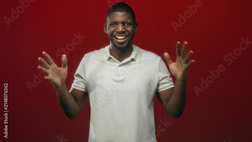 Photography Man raises hands palms open and smiles in studio against a solid red backdrop, shifting from guarded fists to open palms across shots; joyful playfulness