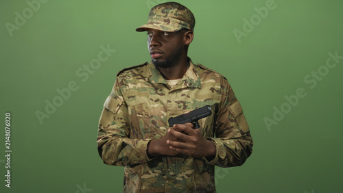 Canvastavla Man soldier in camouflage uniform and cap holding pistol with both hands in a studio green screen setting; duty focus vigilance
