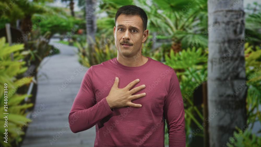 Fototapeta premium Hispanic man with mustache, hand on chest on boardwalk path, wearing maroon long sleeve shirt and looking earnest; sincerity gratitude.