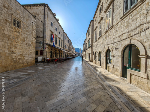 Historic limestone Stradun street in Dubrovnik featuring medieval stone architecture and tourists walking under clear sky.