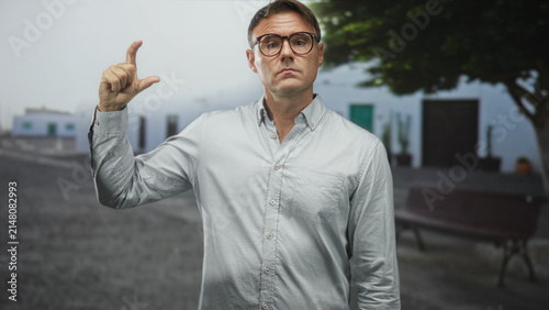 фотографія Man showing a small measurement with his hand in a pinch gesture on a street bench; quiet wry skepticism