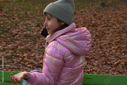 Girl is sitting on a bench in a park talking on the phone with a smile