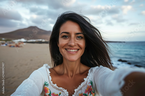 Smiling woman taking a selfie on the beach with a mountain in the background
