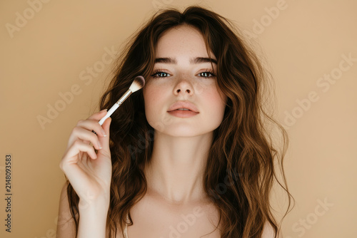 Woman applying makeup with a brush in front of a neutral background
