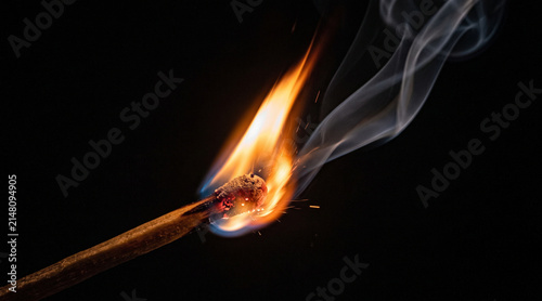 Burning matchstick with bright flame and smoke, isolated on dark background.