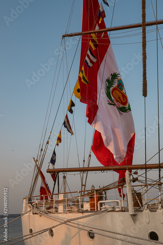 Quadro su tela Ship displays red and white flag with symbols at sunset on calm water