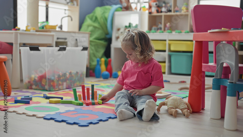Konstfotografi Girl on hands and knees playing with foam puzzle mat, stacking blocks and doll inside a playroom building; playful curiosity