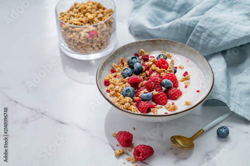 Natural greek yogurt with granola, blueberry and raspberry in a bowl on a marble background
