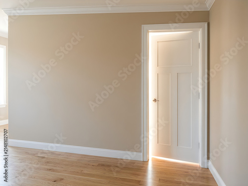 Open white door in a minimalist room with beige walls