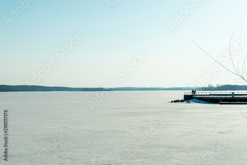 Bild auf Leinwand Quiet winter scene at a frozen lake with a person on a dock enjoying the view of